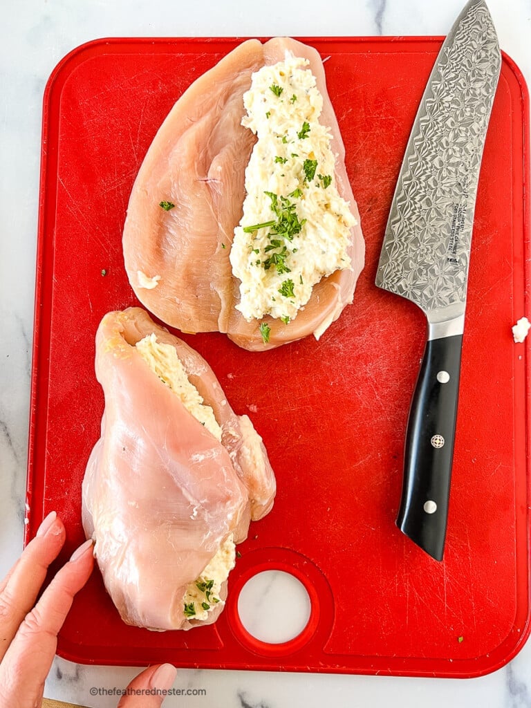 Unbaked cheese stuffed chicken breast on a cutting board.