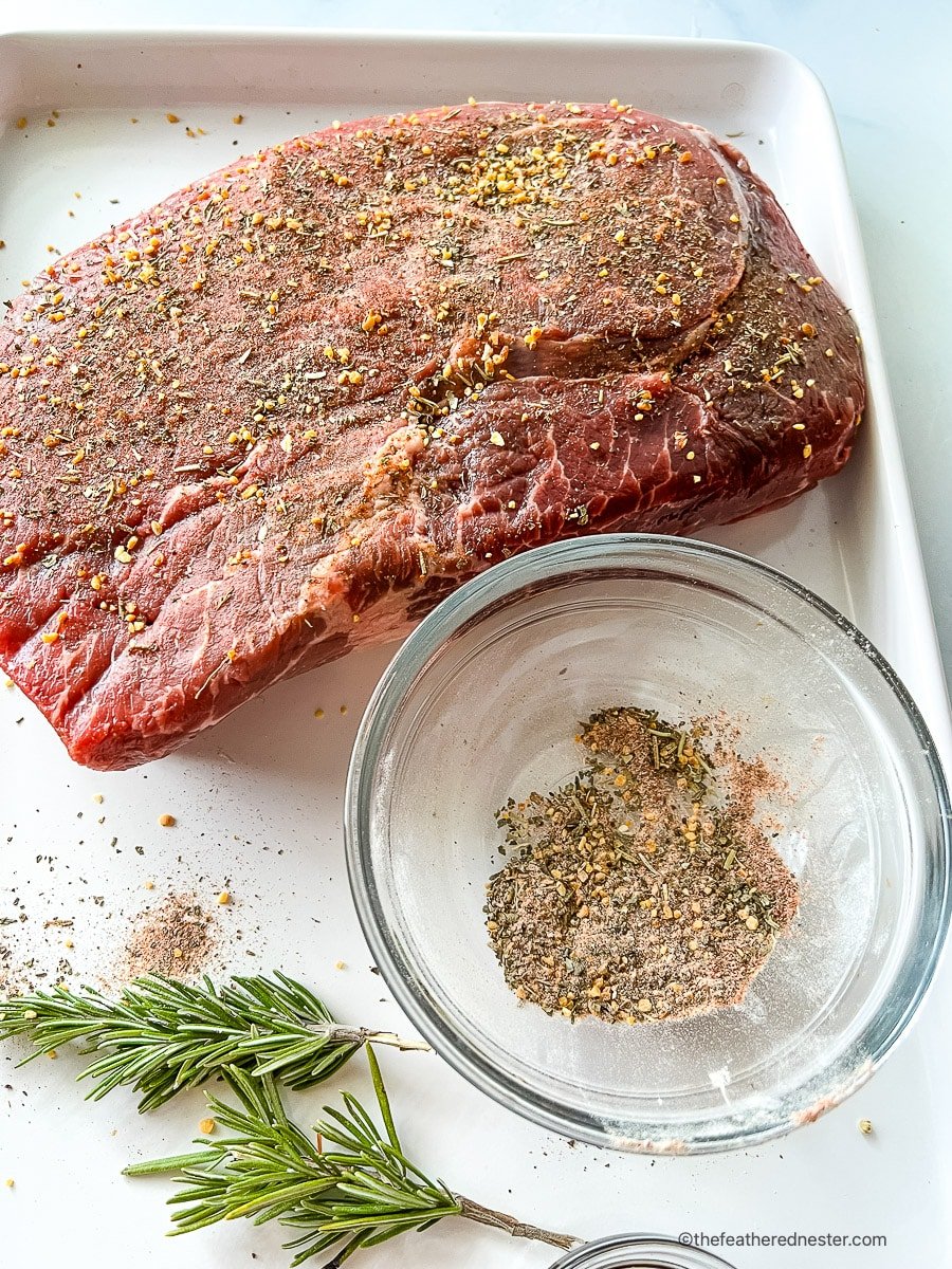 Three pounds of seasoned boneless sirloin roast next to small bowl of dried seasoning.