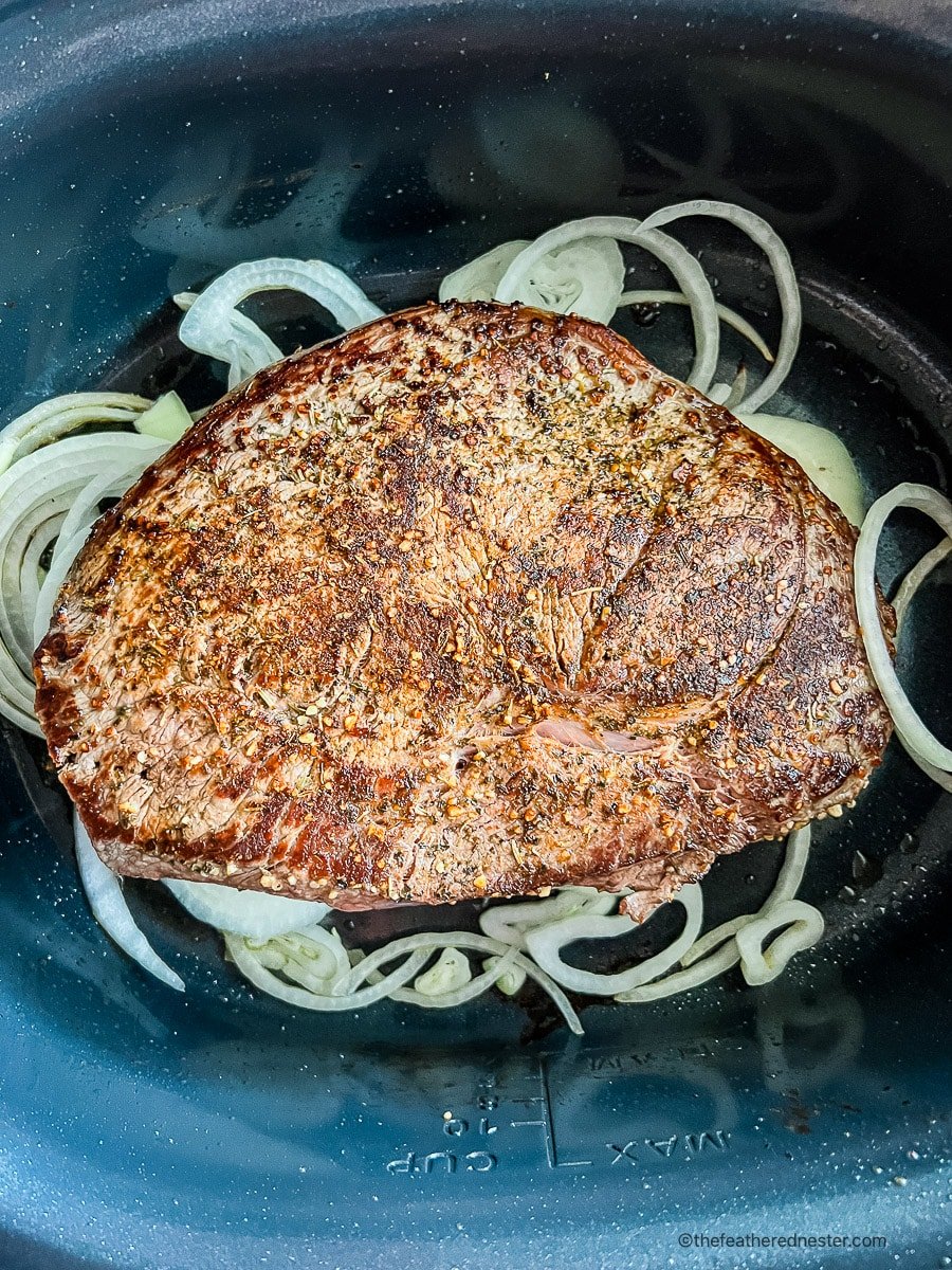 Seared meat in crockpot with raw onion slices.