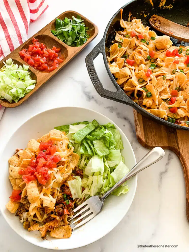 Walking taco casserole on a white dinner plate and in a skillet next to the plate.