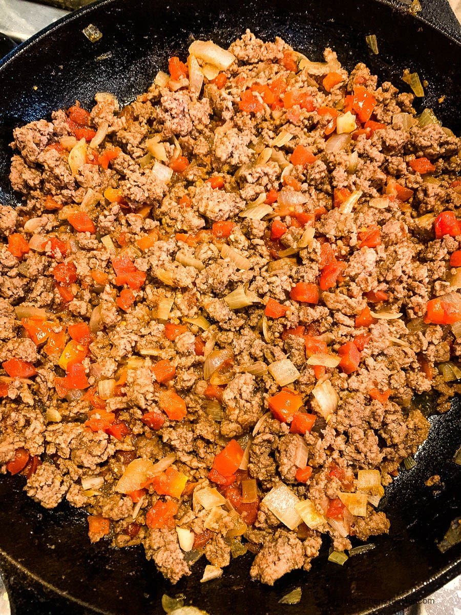 browned meat with tomatoes and onions in a pan.