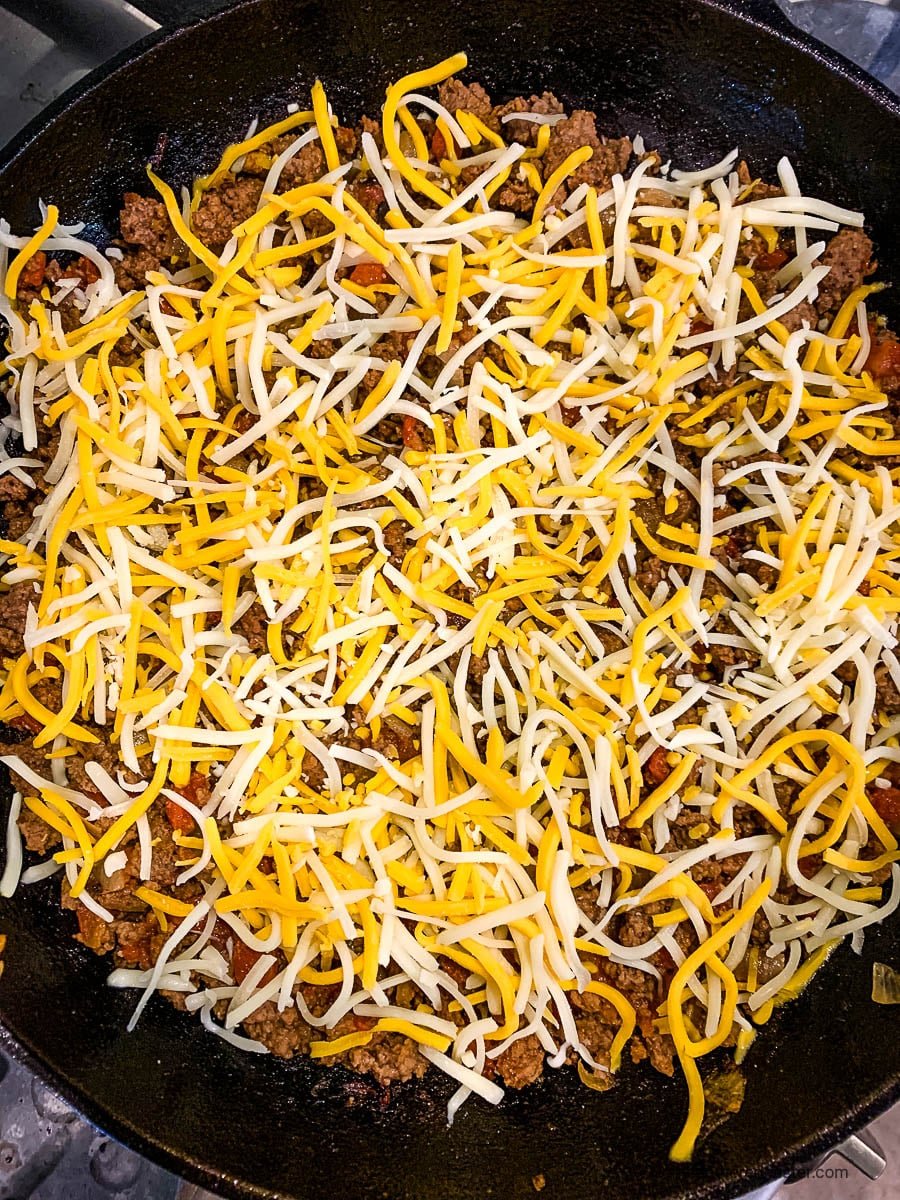 shredded Mexican cheese blend over cooked taco meat in a skillet.