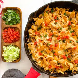 Walking taco casserole with Fritos in a skillet and dishes with toppings on the side.