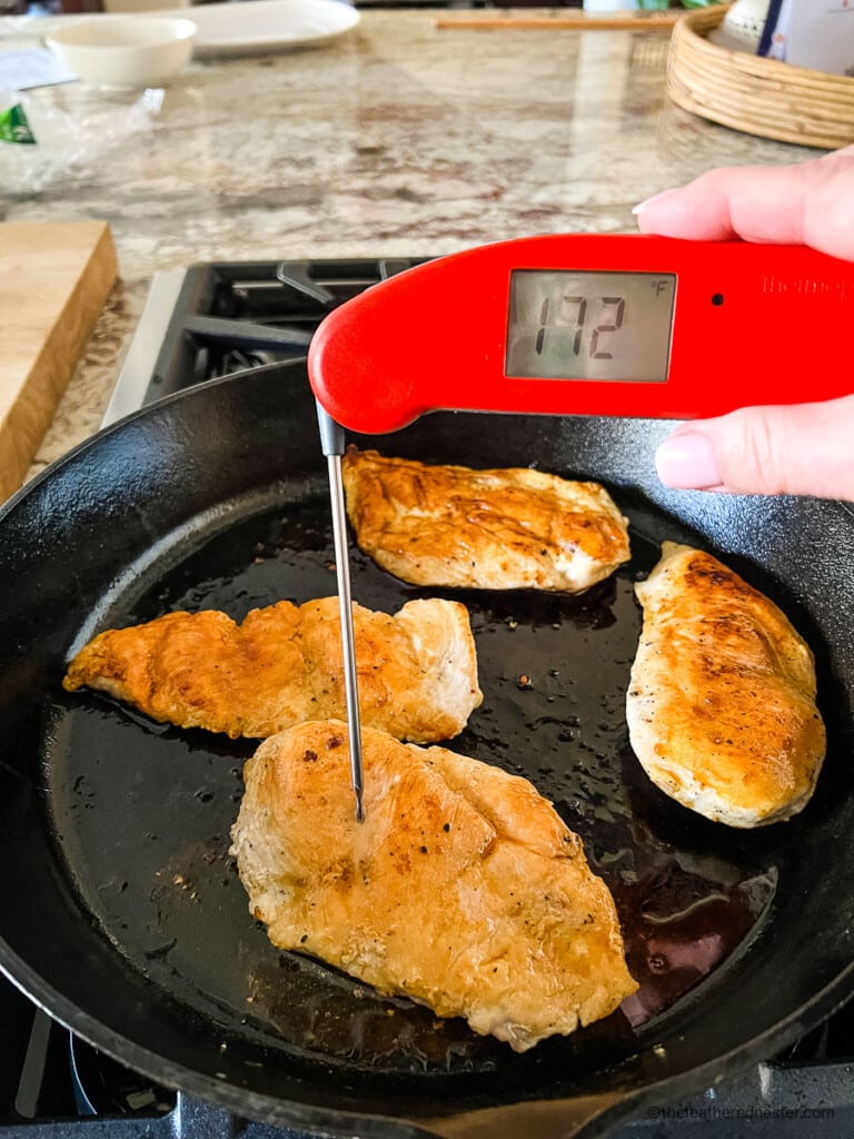 Using an instant read digital thermometer to measure internal temp of boneless chicken breast.