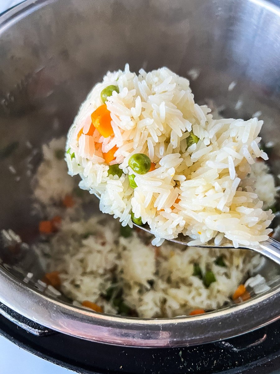 Vegetable rice pilaf on a serving spoon with pressure cooker beneath it.