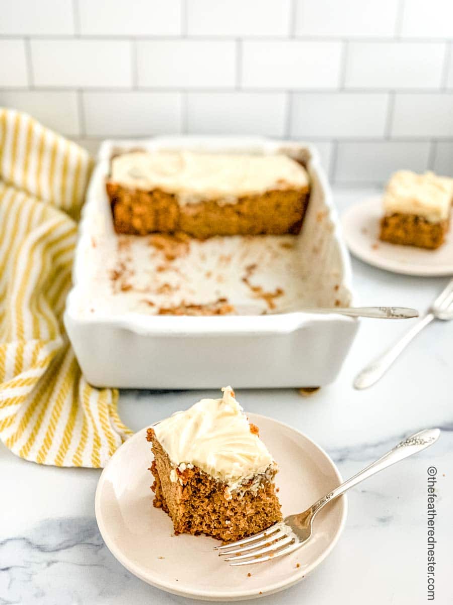Serving of frosted cake and a fork on a white plate.