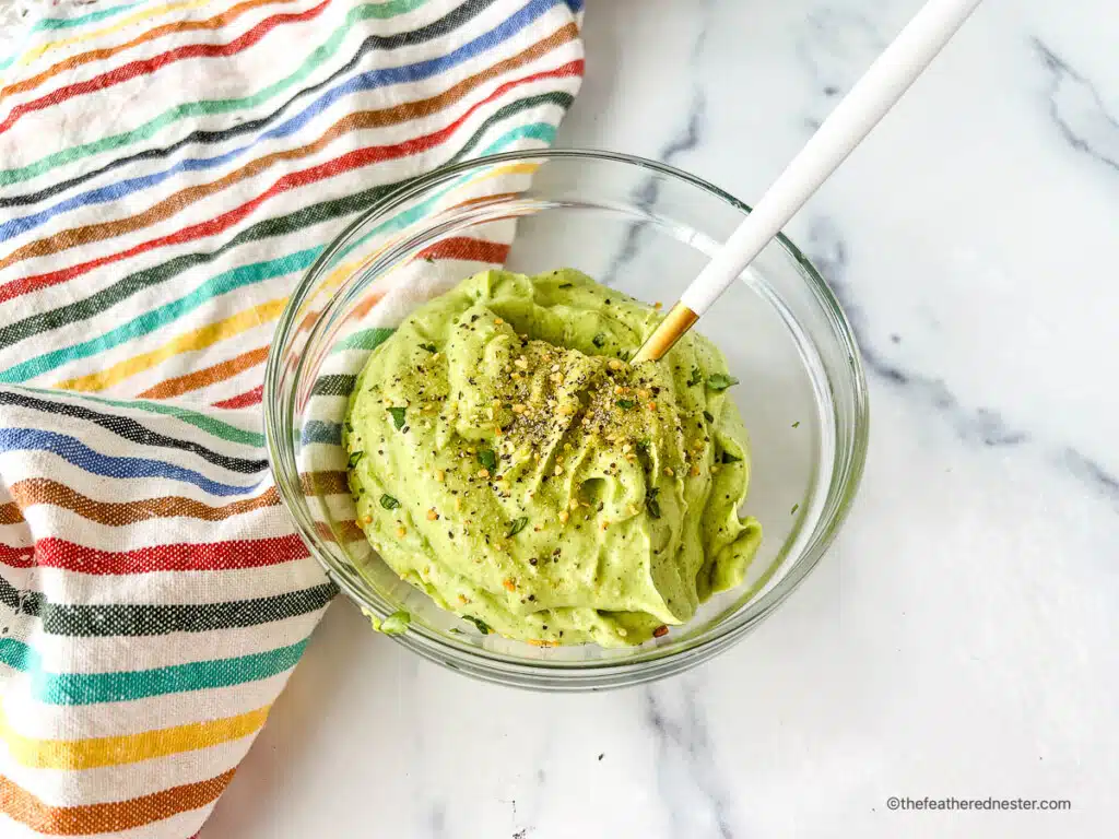 Avocado cream sauce in a clear glass bowl with serving spoon.