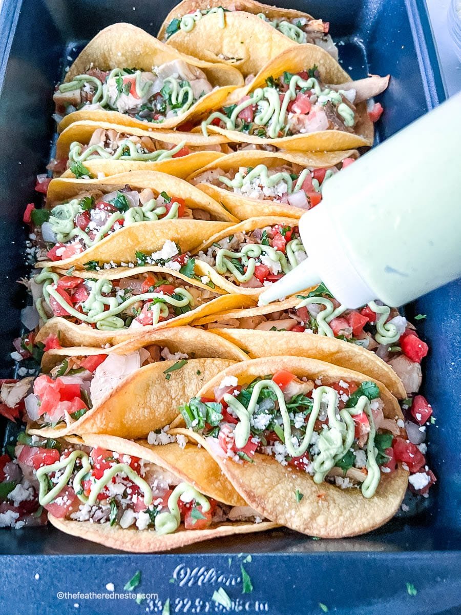 Garnishing a platter of tacos with fish taco sauce.