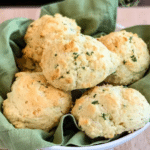 Jalapeno biscuits in a white serving bowl lined with a green kitchen towel.