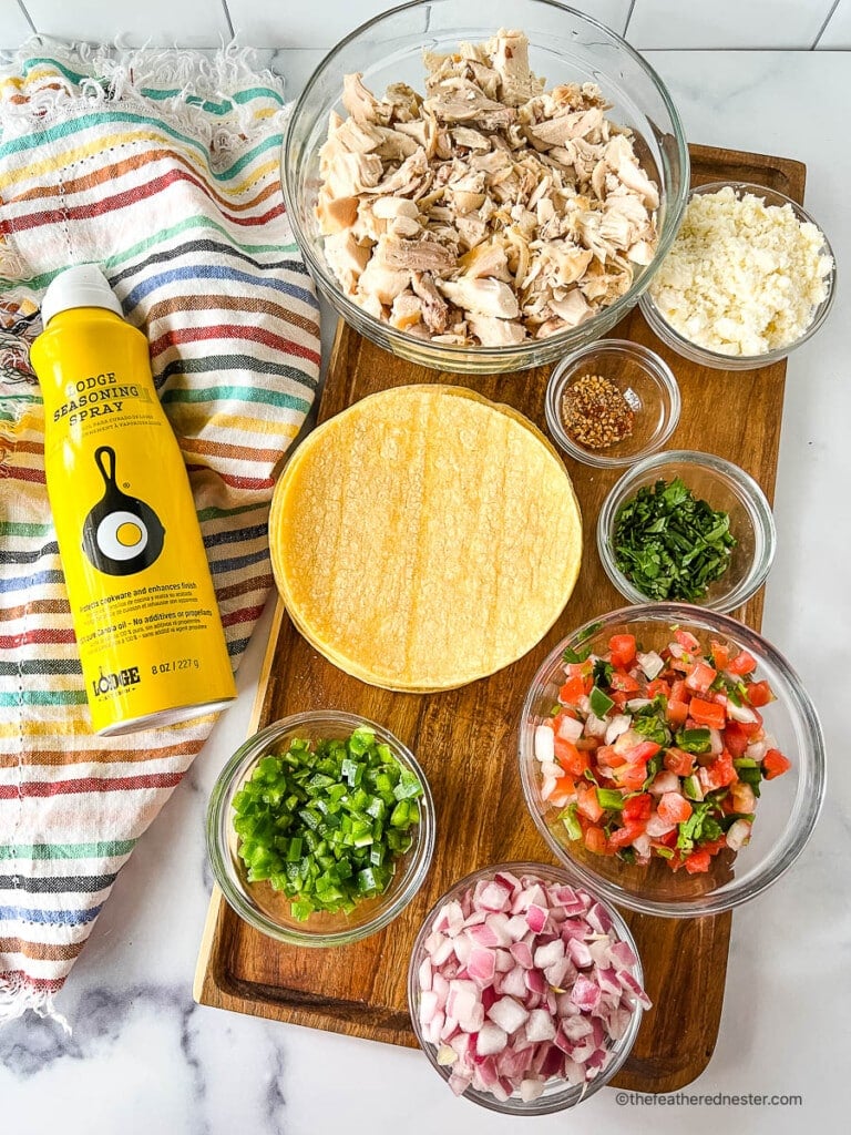 bowls of ingredients for a chicken street taco recipe on a wooden board next to a striped kitchen towel and non-stick cooking spray.