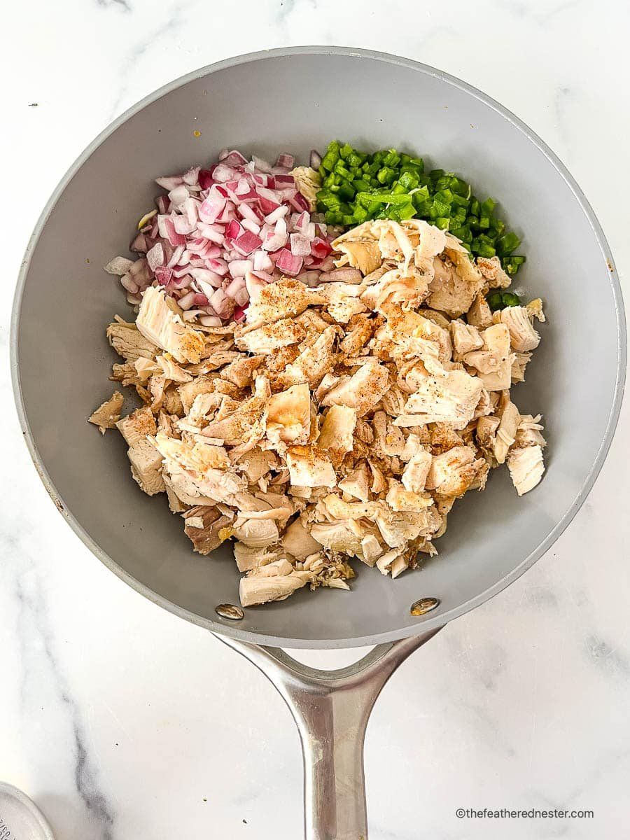 Diced red onion, chopped cilantro, and cooked chicken breast in a skillet.