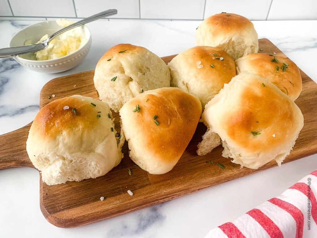 Small dish of butter next to soft homemade bread on a wood serving board.