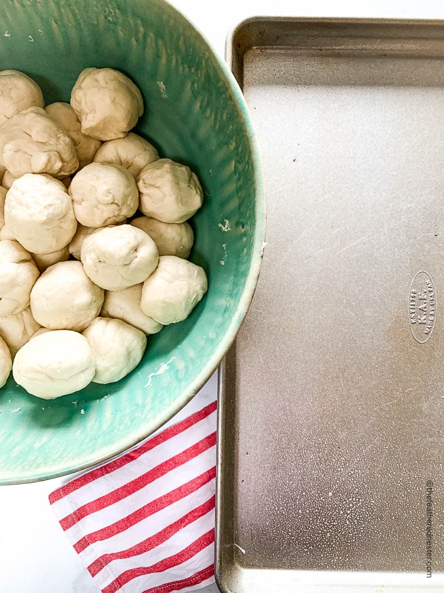 Bowl of unbaked potato rolls next to a sheet pan.