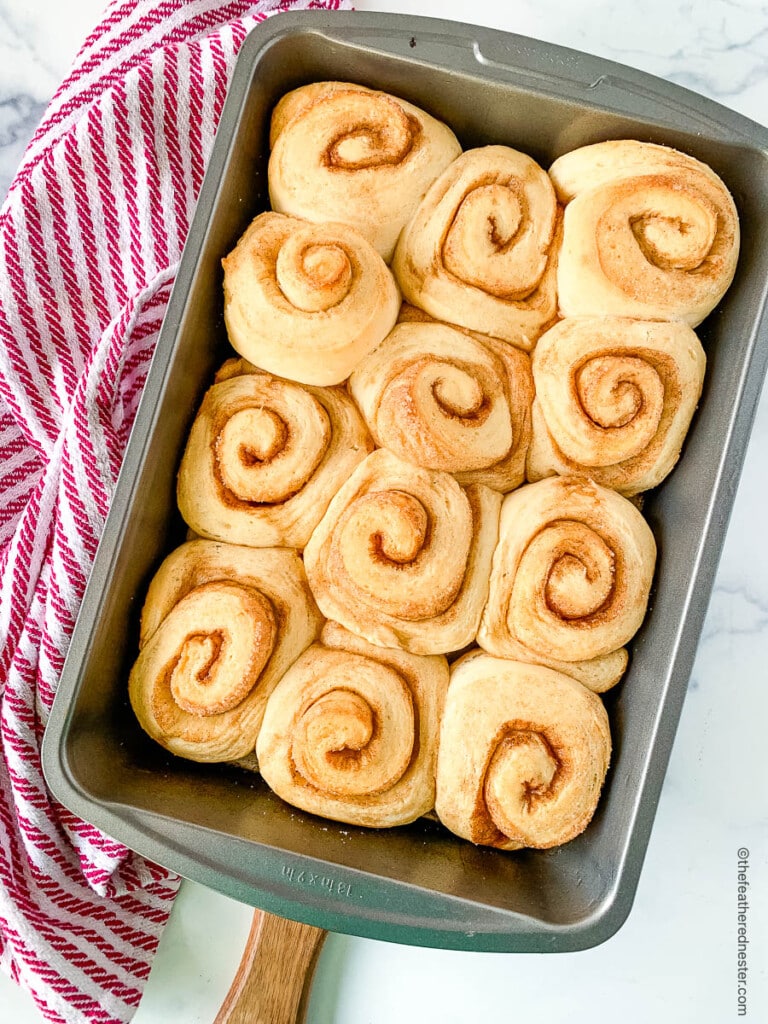 Sweet breakfast buns in a baking pan on counter next to a kitchen towel.