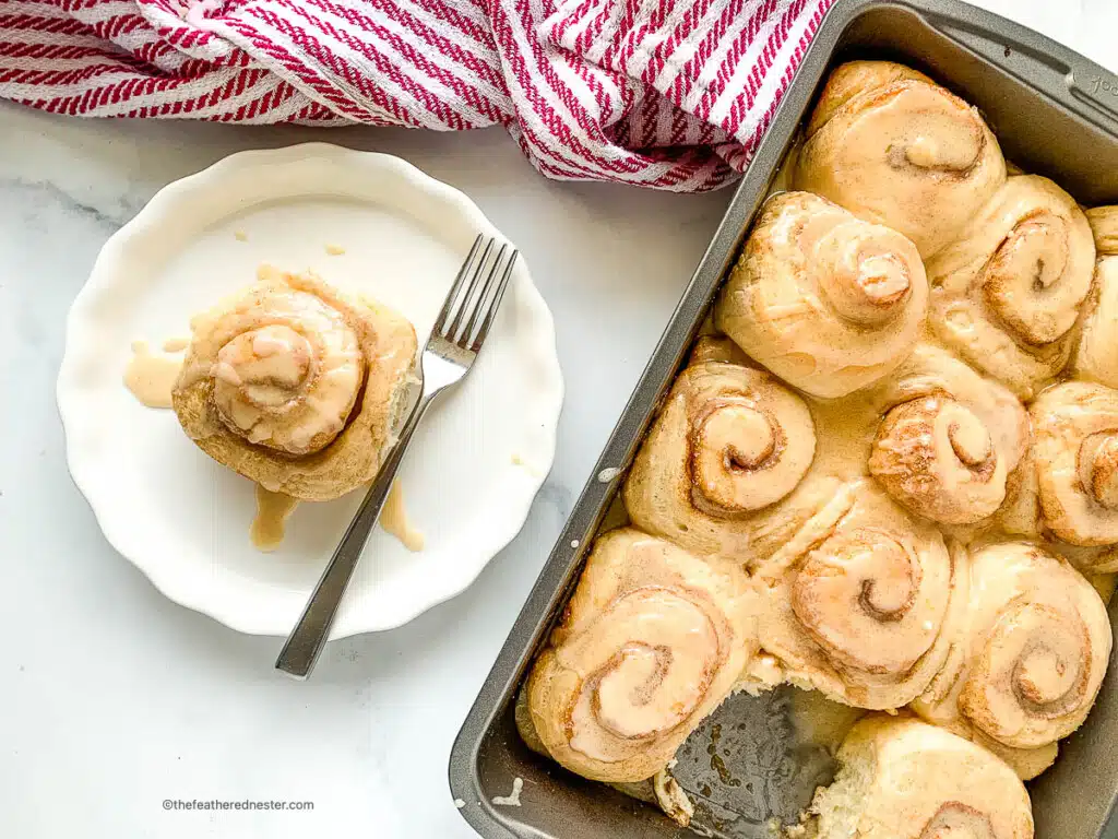 Frosted sourdough cinnamon rolls in a baking pan next to a plated cinnamon roll.