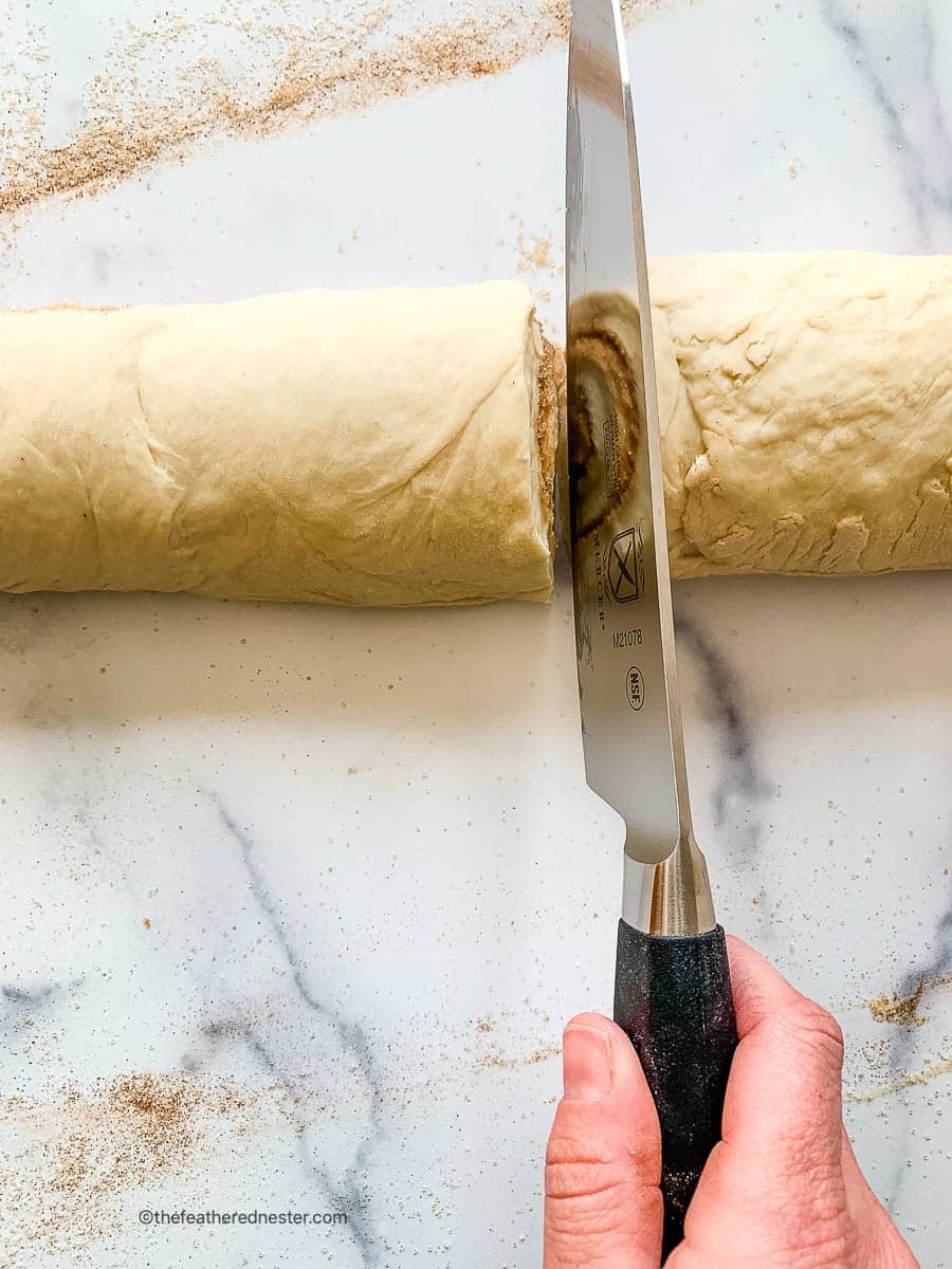 Chef's knife slicing into dough for sourdough discard cinnamon rolls.