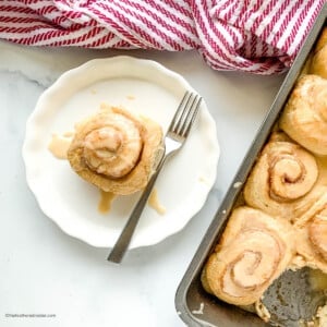 A fork and cinnamon bun on a round white plate.