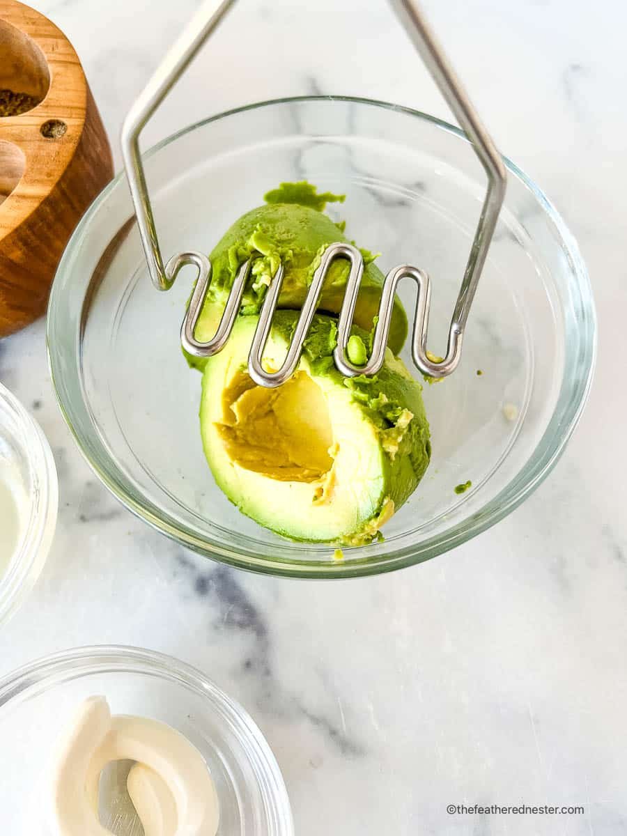Using potato masher to smash green fruit in a bowl.