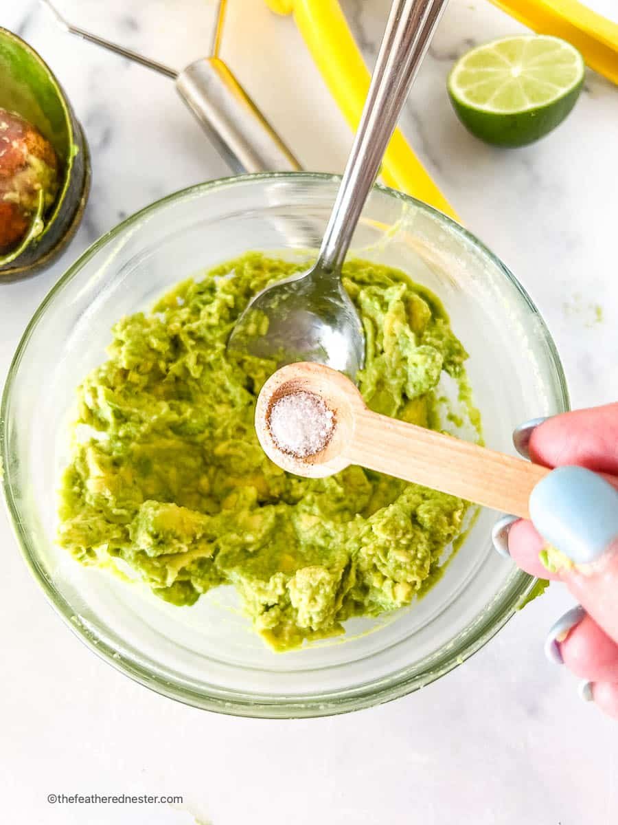 Adding teaspoon of salt to a bowl with creamy guacamole spread.