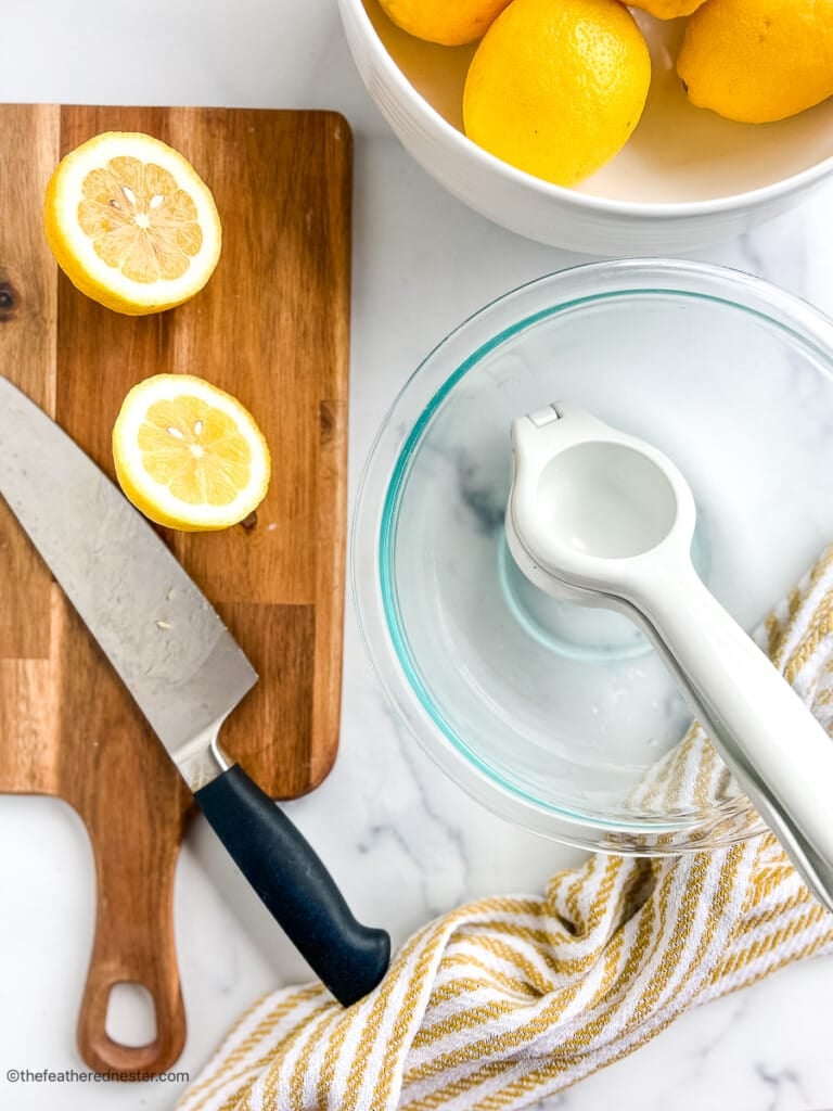 chef's knife on a cutting board next to a large glass bowl with a citrus press.