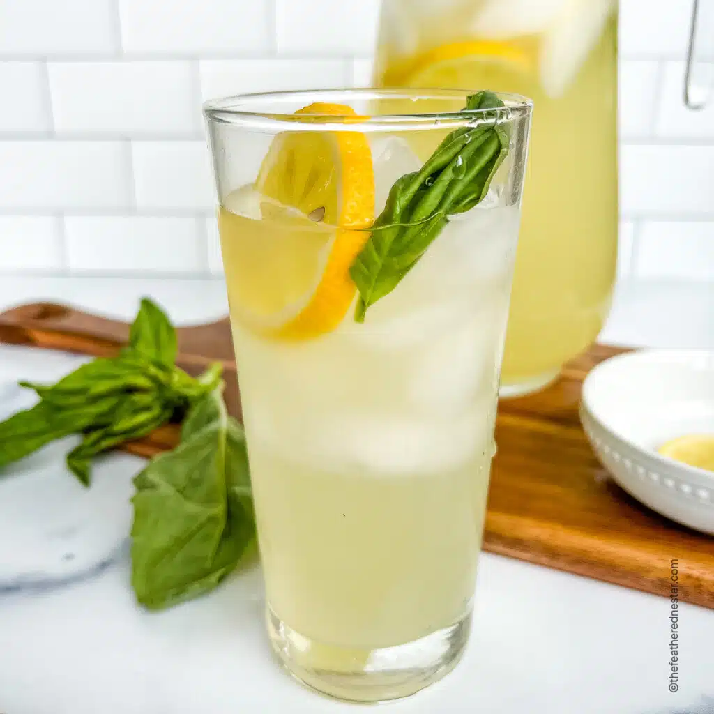 Freshly made basil lemonade served over ice in a tall drinking glass, garnished with basil leaves and a lemon slice.