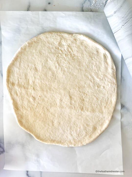Unbaked Bisquick pizza dough rolled out on a sheet of parchment paper.