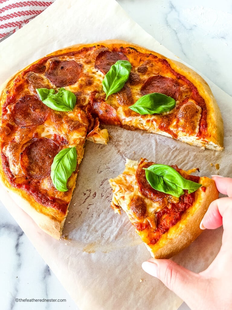Woman's hand removing slice of homemade pepperoni pizza.