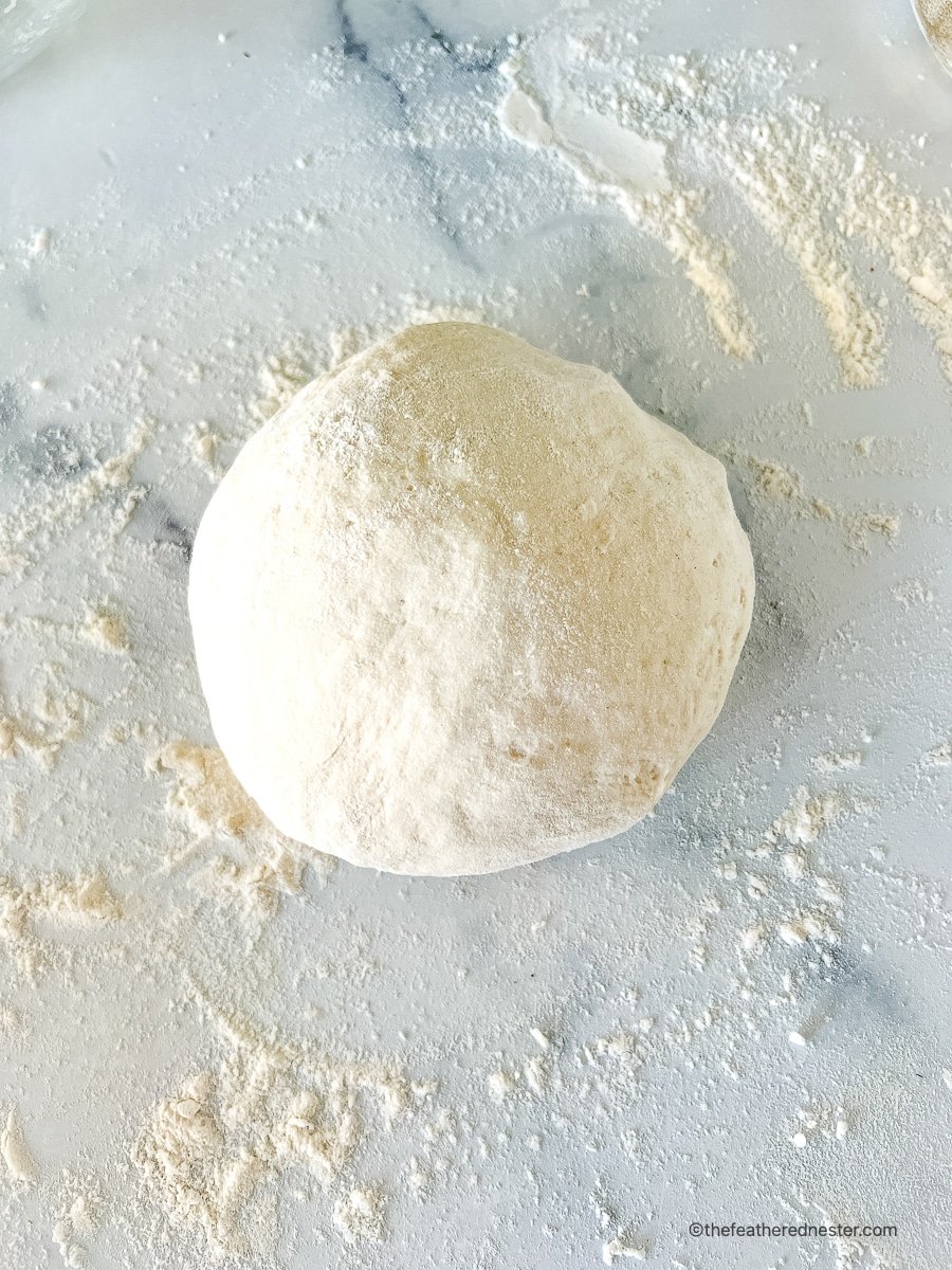 Ball of pastry on floured marble surface.