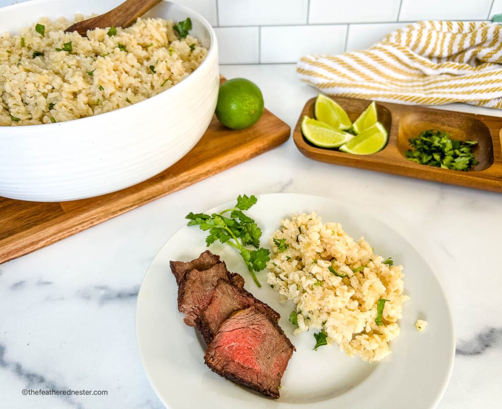 Chipotle brown rice and beef on a dinner plate next to dish with lime wedges and chopped cilantro.