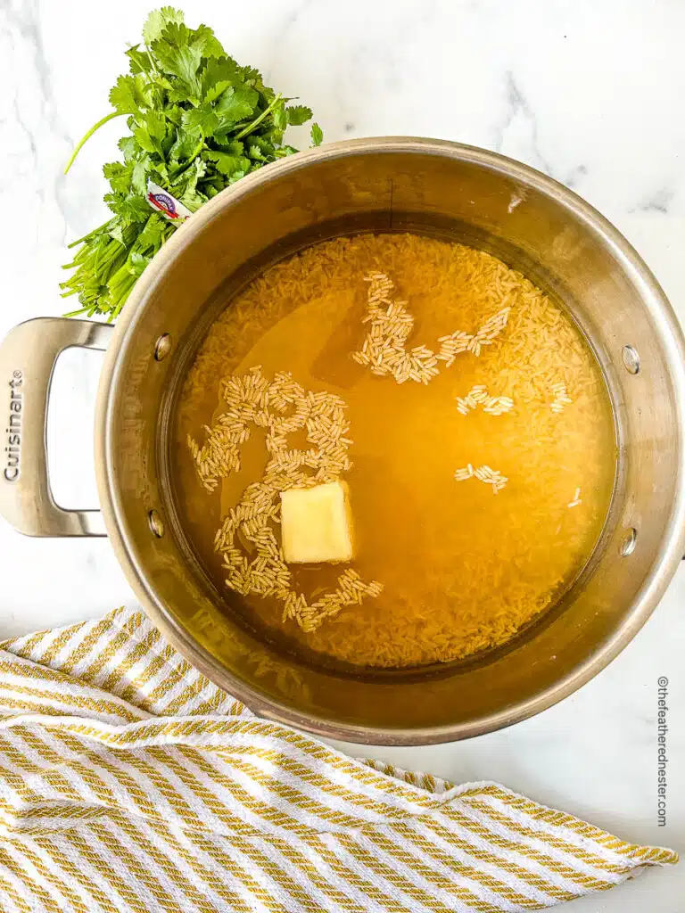 Overhead view of large stock pot with chicken stock, butter, and uncooked brown Basmati.