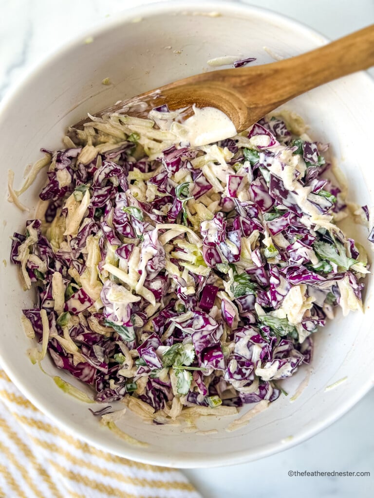 Mixing chopped red cabbage and cukes with creamy dressing in a large bowl.