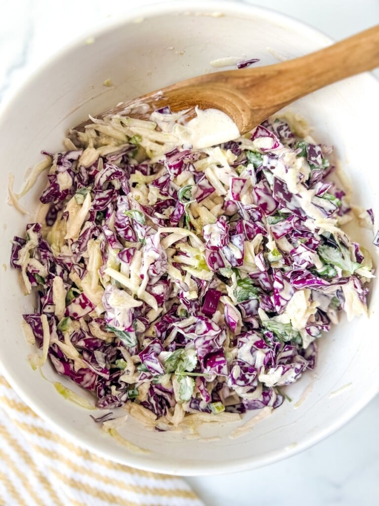 Wooden spoon in a white bowl of cucumber slaw.