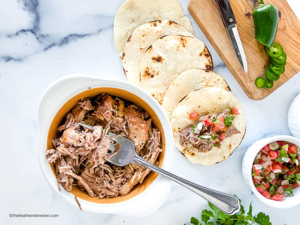 Juicy, fork tender Dutch oven carnitas in a small bowl and on tortillas.