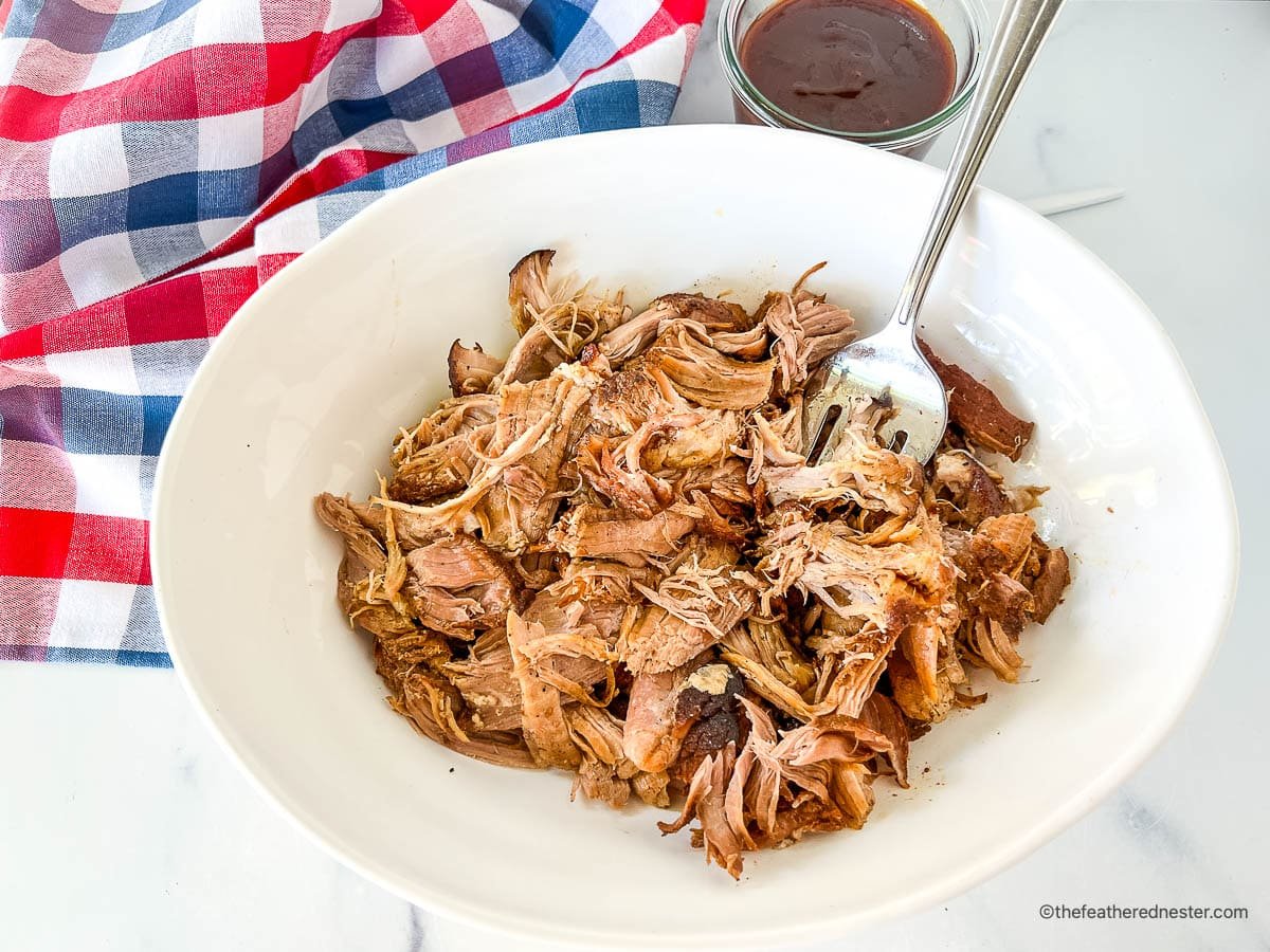 Bowl of pulled pork in serving bowl with large fork.