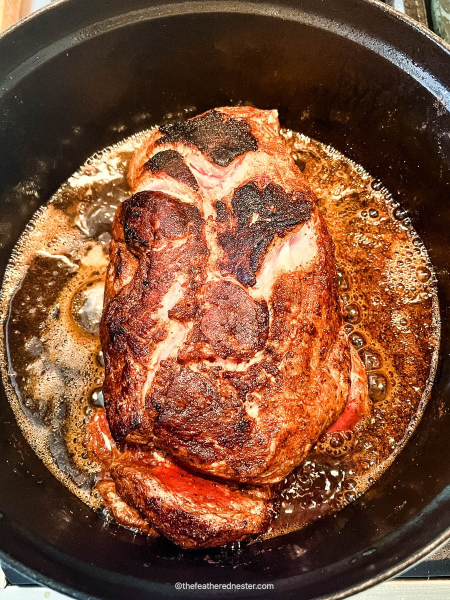 Perfectly seared Dutch oven pork roast in pot of meat juices.