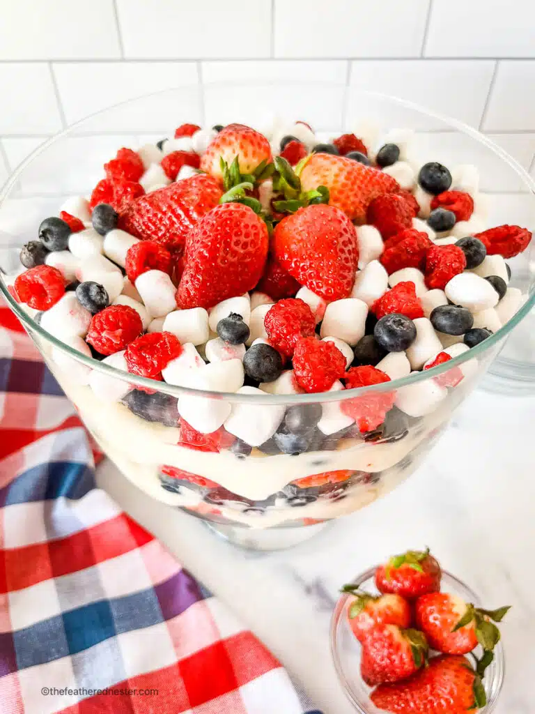Layered red white and blue fruit salad on a table next to red white and blue checked kitchen towel.