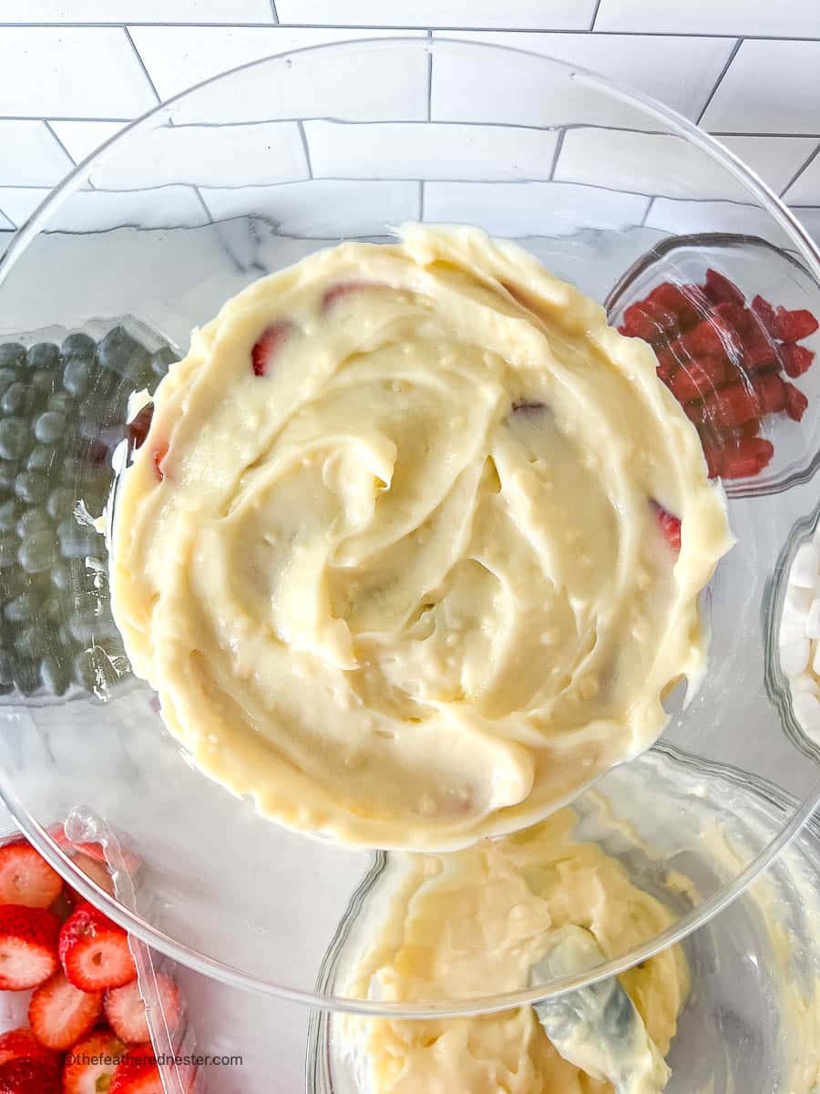 overhead: layer of white pudding over red and blue berries in a bowl.