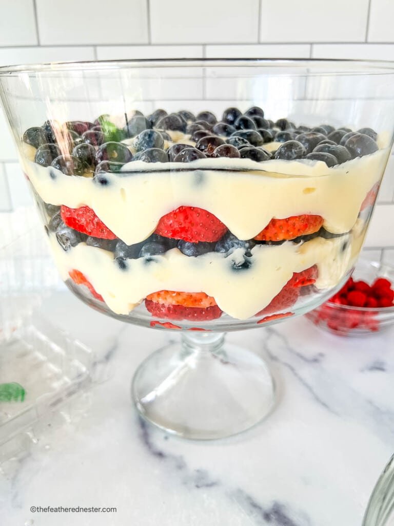 Layered fruit and pudding 4th of July salad in a trifle bowl.