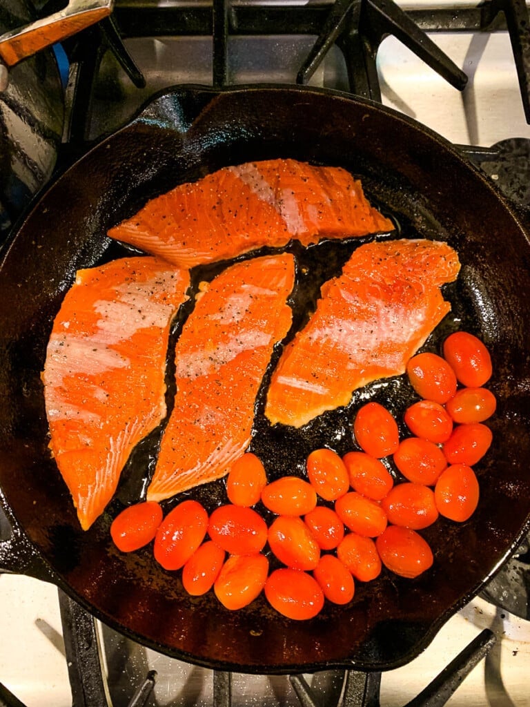 Pan frying fish and cherry tomatoes in a cast iron skillet.