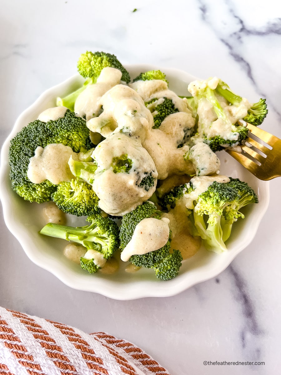 Bowl of Instant Pot steamed broccoli with cheese sauce, and one floret on a fork.