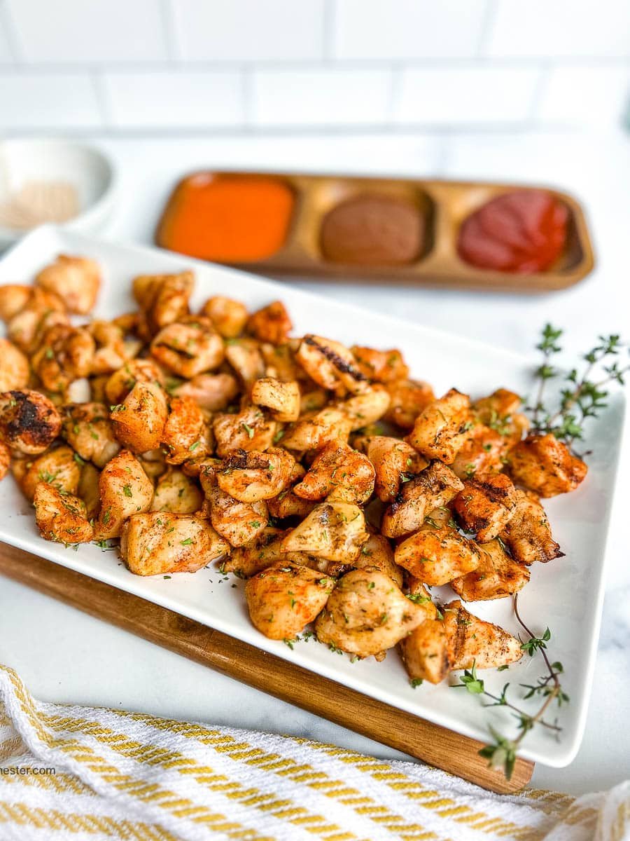 Grilled chicken nuggets on a serving platter next to dipping sauces.