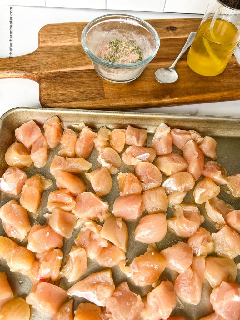 Bite sized pieces of uncooked boneless skinless poultry spread out on a baking sheet.