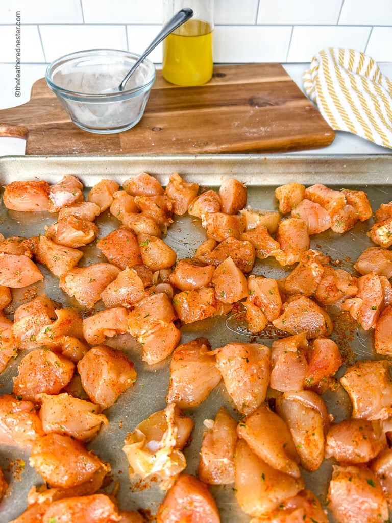 Bite sized pieces of seasoned chicken breast spread out on a baking sheet.