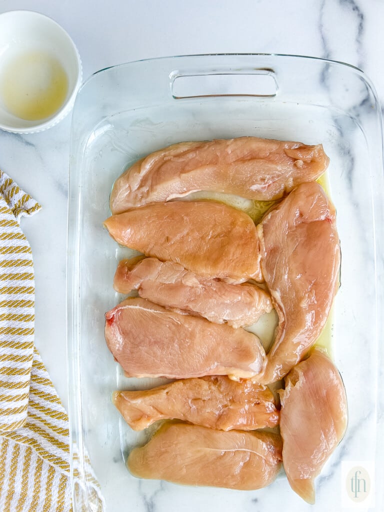 Uncooked thin chicken breast pieces in a baking dish.