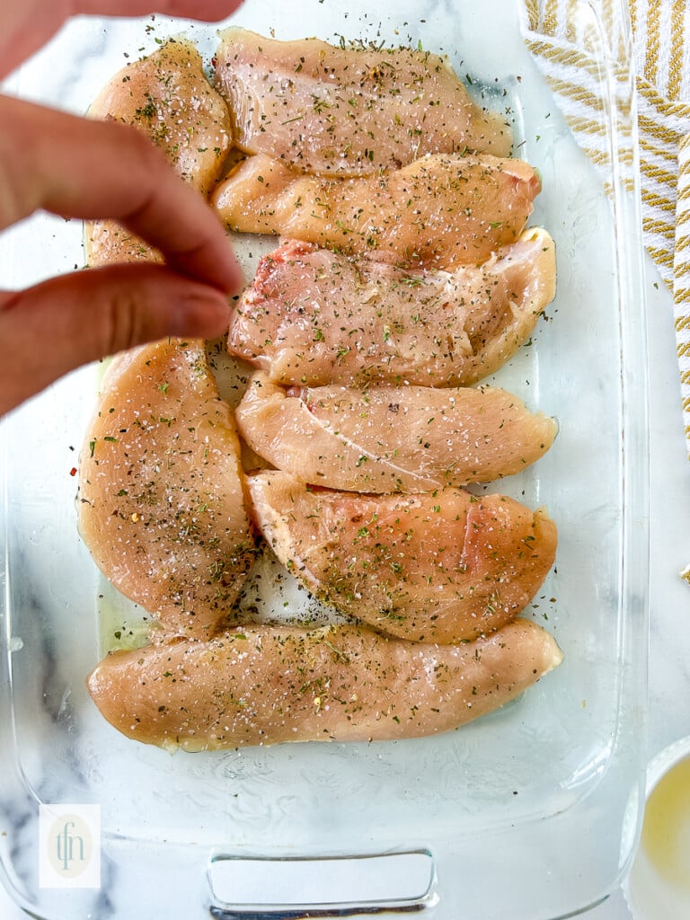 Hand sprinkling salt and pepper over pieces of raw poultry.