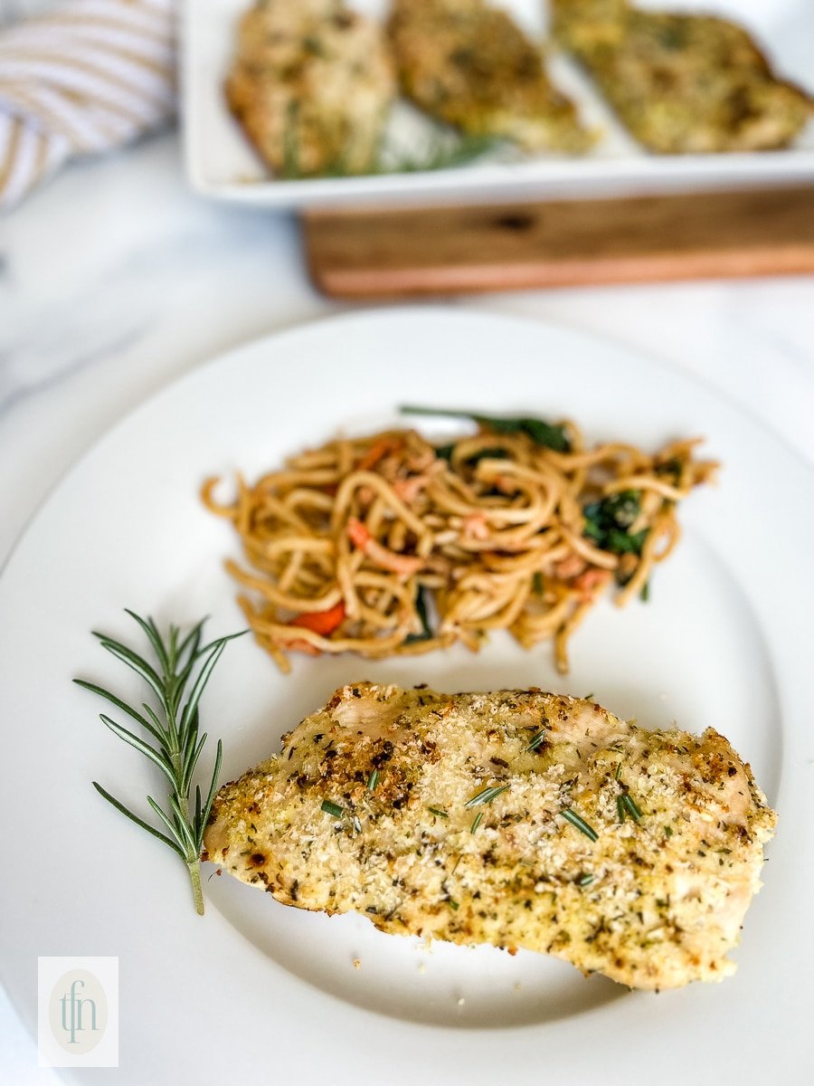 Baked lemon pepper panko crusted chicken breast on a plate with cooked pasta.