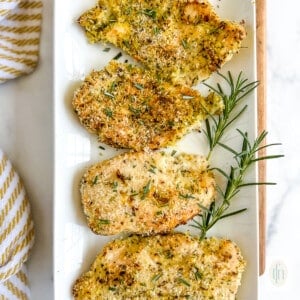 Four panko breaded chicken breasts on a white serving platter.