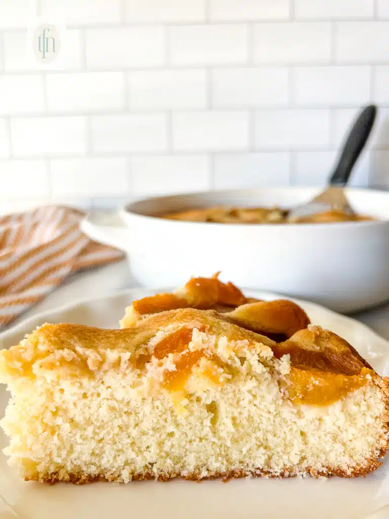 side view: plated slice of moist cobbler cake topped with fresh peaches.