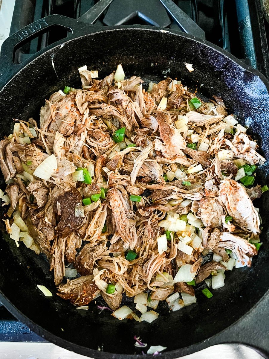 Cooking leftover pulled pork in a skillet with diced jalapenos and onions.