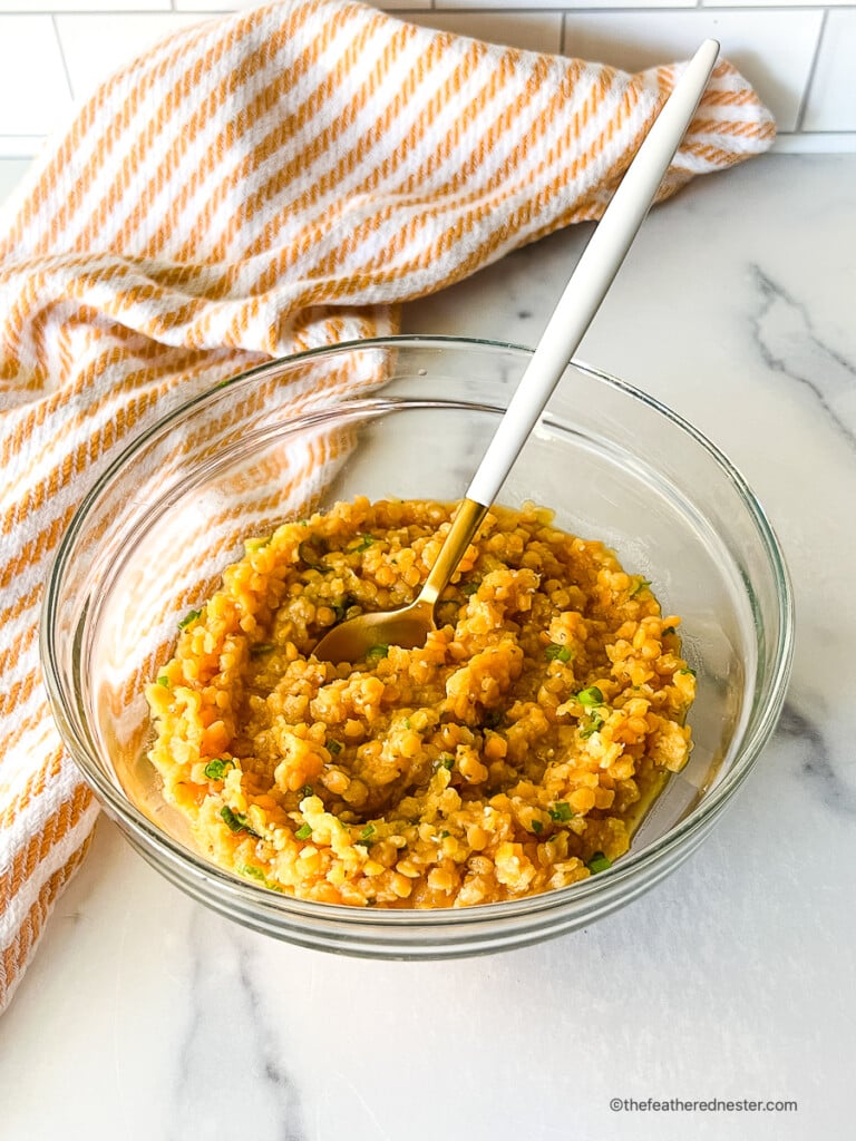 Red lentils in a small, clear glass dish with a white serving spoon.